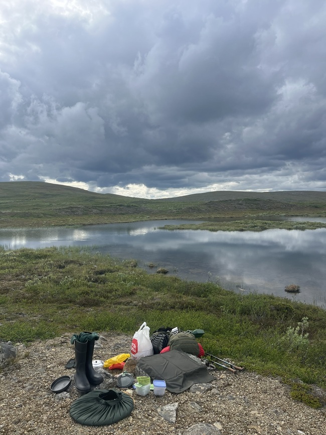 Picture shows cooking utensils and equipment next to a lake. Sky is filled with very dark clouds.